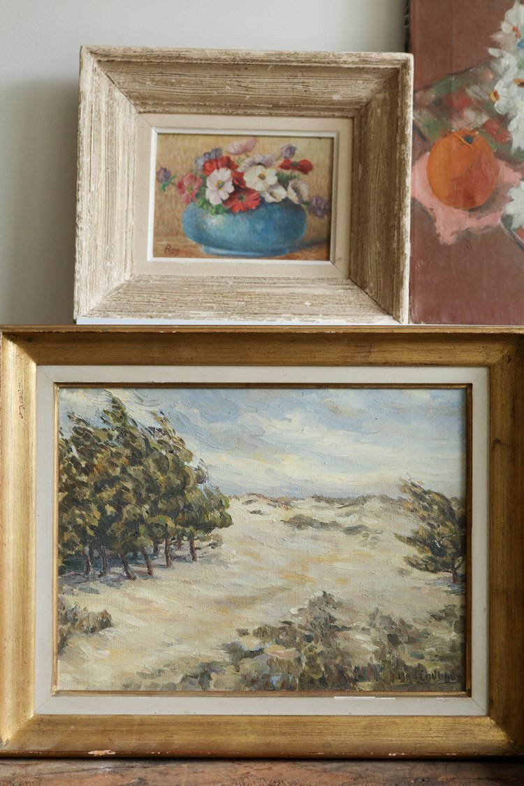Two framed paintings on a wall; one with flowers and the other with a landscape.